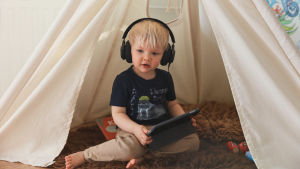 Pieni lapsi kuulokkeet korvilla kuuntelee ohjelmia älylaitteelta.