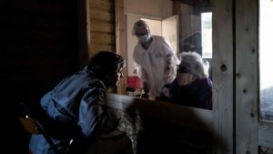 Äldreboende i Frankrie ger möjlighet för anhöriga att möta de äldre. En kvinna talar med sin mor och vårdare med munskydd bakom glasruta på äldreboende i Frankrike