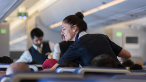 Politikerna vill trygga arbetsplatser, Lufthansaledningen är skeptisk. Två flygvärdar pratar med kunder i ett långdistansflyg.