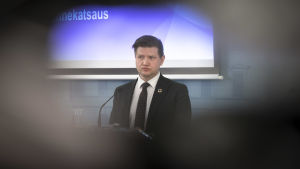 Mikko Koskinen står vid ett talarpodium. 