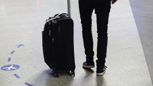 En person som har en lite kappsäck bredvid sig. Bara mänskans fötter och rygg syns.