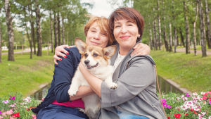 Ett husdjur skänker mycket värme och glädje till sina ägare. Två kvinnor sitter bredvid varandra utomhus. De har armarna om varandra och om en hund som de har i famnen.
