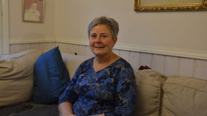 Gudrun Degerth tycker det är fint att många av de Nynagubor som flyttat bort från Nagu fortfarande håller kontakten och hälsar på. Medelålders kvinna i soffa.