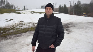 Ville Rissanen hoppades före nyår att backen snart skulle vara täckt med snö istället för med grått slask som syns i backen bakom honom. En man i medelåldern som står i en skidbacke