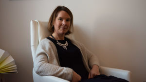Anna Collander säger att den rehabiliterande psykoterapin fungerar bra under FPA, det är i den primära mentalvården som problemen skapats. En kvinna sitter i en vit fåtölj, vägg i bakgrunden.