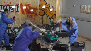 Här slås allt sönder. Tre människor står och slår sönder saker med yxor och metallstänger.