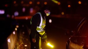 Endast arbetsresor är tillåtna från de isolerade områdena En polisman i skyddsdräkt bredvid en stoppad bil