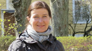 Nina Fredriksson är i Hangö eftersom hon inte på grund av sitt jobb måste vara nära flygplatsen. Nu blir hon permitterad, men vill inte bli sysslolös. En kvinna med brunt långt hår, fäst i hårsnodd bak. Står ute i solsken. Vår, en gul träfasad och några lönnar i bakgrunden. Hon ler.
