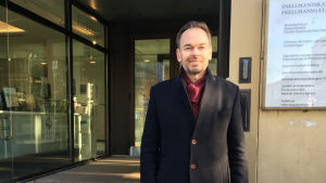 Folktingets sekreterare Markus Österlund. Man vid ingång till kontorshus i Helsingfors