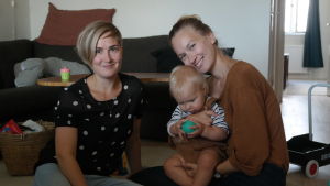 Folkhälsans doulakoordinator Liisa Jungar (till vänster) tillsammans med mamman Inka-Maria Pulkkinen som använt sig av en doula. Doulakordinator Liisa Jungar sitter på golvet hos Inka-Maria Pulkkinen och hennes son Gabriel Nyman