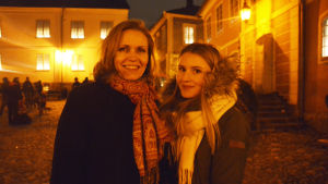 Lena och Matilda Törnqvist. En medleålders kvinna och en yngre kvinna står bredvid varandra och ler. De står utomhus på ett torg i det gula skenet av gatlampor.