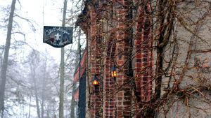 Kända arior framförs på Slottskrogen i april. En röd tegelbyggnad med lyktor vi dörren. En gammaldags skylt där det står Slottskrogen. Träd i bakgrunden.