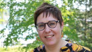 Henrika Nordin. En kvinna med glasögon och kort mörkt hår står framför en björk.