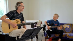 Ari Siikasaari lär eleven Luka Wennervirta grunderna i gitarrsolon iTrägårdsmästaren stuga. En man och en pojke sitter med varsin gitarr