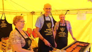 Kerstin Söderlund, Arne Erlands och Henry Söderlund säljer korv. En kvinna och två män står och säljer korv i ett tält.