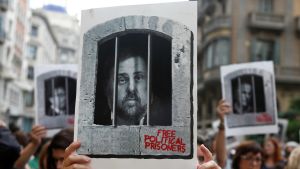 Under protester i Barcelona höll demonstranter upp skyltar som föreställer den tidigare katalanska vice regionpresidenten Oriol Junqueras bakom galler. Junqueras dömdes av Högsta domstolen i Spanien till 13 års fängelse. En demonstrant håller upp en skylt som föreställer den tidigare vice regionpresidenten i Katalonien Oriol Junqueras som dömdes till 13 års fängelse.
