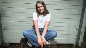 Nadya Mattsson. Nadya sitter på en stubbe med benen i kors och ler mot kameran