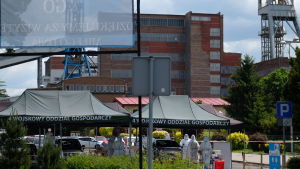 Masstestning av gruvarbetare i juni i södra Polen. En röd flervånings tegelbyggnad med ställningar med metallvinschar på varsin sida om sig. Framför byggnaden svarta tält med polsk text och människor i vita skyddskläder samt parkerade bilar.