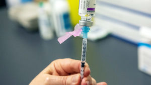 Astra Zenecas vaccinflaska som någon tar vaccin ur med en spruta.
