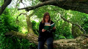 Kaisa Pulakka istuu puussa ja lukee Ronja, ryövärintytärtä