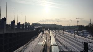 Snön från tågbanan mellan Böle och Helsingfors centralstation smälts på ett uppvämt fält i Ilmala. Tåg i Böle i vintersol.