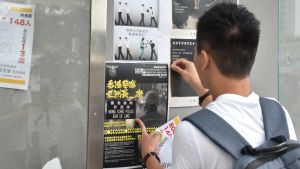 John Ng fäster en affisch som fördömer polisen på en så kallad demokrativägg vid Hongkongs äldsta universitet. En Honkongbo sätter upp planscher.