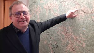 Greger Forsblom. En man med glasögon pekar på en väggkarta över Pedersöre