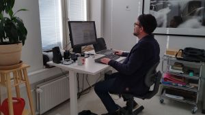 Torsten Colérus jobbar ibland hemifrån och ibland från Spinneriet. Hans företag finns i Åbo där han har sina kollegor. En man som sitter vid en dator i ett öppet kontorslandskap. Han har mössa på huvudet, ryggen vänd mot kameran.