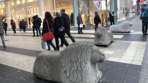 De gamla betonglejonen väger 900 kg och har kritiserats för att inte vara tillräckligt tunga. Stockholms stad utreder att skaffa ännu tyngre betonglejon. Alla 130 beställda lejon har ännu inte levererats. Tre betonglejon på Drottninggatan i Stockholm.