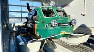 Hydrokoptern kom till användning. Fordonet kan köra både på is och vatten. En grön hydrokopter. Fordonet har pontoner som medar och en motor bak på.