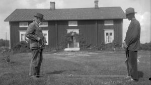 Två män leker "dra girsnot", där man ska försöka få omkull sin motståndare genom att dra i ett rep som är fastspänt mellan de tävlandes vrister. Bilden är tagen 1930 i Finström, Åland.