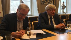 Mikko Hupa, rektor för Åbo Akademi och Kalervo Väänänen, rektor för Åbo Universitet skriver under avtalet. rektorerna för åbo akademi och åbo universitet skriver under ett avtal