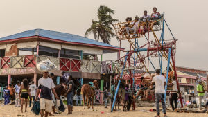 Nigeria går i motsatt riktning. Strand i Nigeria som kryllar av människor. På bilden syns hus och ett hemgjort litet pariserhjul.