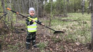 Oliver Sundvik med krattan i högsta hugg. En liten pojke står och krattar med en kratta som är dubbelt längre än han själv.
