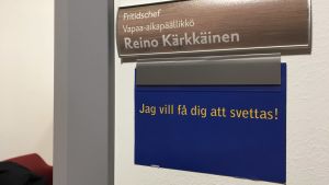 Här går man in i fritidschefens rum. Skylt på väggen där det står fritidschef Reino Kärkkäinen och under det "Jag vill få dig att svettas".