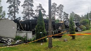Gulröda band har placerats runt det branddrabbade huset. En radhuslänga som brunnit, en vit tegelvägg och svarta bräden finns kvar.