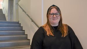 Janice Mattlar. En kvinna med långt ljusbrunt hår och glasögon står i en trappuppgång.