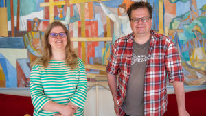 Museichef Laura Lotta Andersson och arkeolog Jan Fast. Museichef Laura Lotta Andersson och Arkeolog Jan Fast står framför en färggrann tavla på Hangö museums kansli.