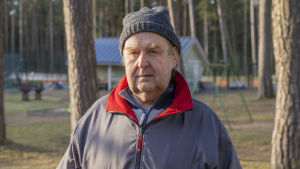 Hangö stadsstyrelse har nyligen godkänt att Hangö tennisklubb får bygga två padelbanor. Det här är bara början på klubbens nya satsningar, säger ordförande Leif Wikström. En äldre man med mössa och blå jacka står ute. I bakgrunden tennisbana och ett klubbhus.