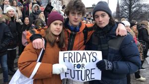 Veronica Winquist och Marcus Schramko, från Lärkan, flankerar Oskar Bremer från Tölö gymnasium. Tre demonstranter står med ett plakat i handen: Fridays for future.