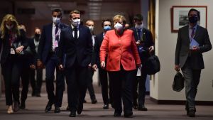 President Emmanuel Macron och förbundskansler Angela Merkel ses som arkitekterna bakom nattens kompromiss. Angela Merkel och Emmanuel Macron går i en mörk korridor i Europabyggnaden. Båda har munskydd.