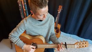 Saarela vill förstå människors liv och lisval genom att skriva låtar om dem. Folksångerska, fotad uppifrån med gitarr i famnen,