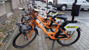 Raseborg stad gör ett försök över sommaren med stadscyklar som man kan hyra via en applikation. Flera orange stadscyklar på rad som folk kan hyra.