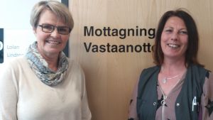 Lolan Lindroos (till vänster) och Eva Hedman hoppas att människor tar kontakt med Raseborgs missbrukarvård också nu under detta coronaläge. Personalen är på jobb och det finns olika möjligheter att mötas, både digitalt och "på riktigt". Två leende kvinnor står mot en stägd dörr där det står "Mottagning Vastaanotto".