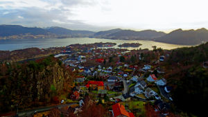Kommunen Askøy ligger på västkusten, granne med staden Bergen. Flygbild över samhälle med havsvik och fjäll i bakgrunden.