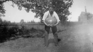 En man lyfter en stor sten med sina händer. Bilden är tagen 1930 i Jomala, Björsby, Åland.