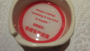 En antitobakskampanj à la Kina. I askoppen konstateras det att det finns en slogan som fastslår att rökning skadar hälsan. Askkopp med slagord mot rökning i Kina.