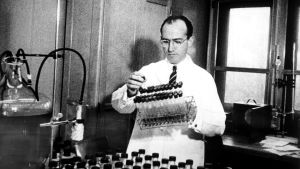 Jonas Salk i sitt laboratorium på 1950-talet. En man i vit rock hanterar provrör i ett laboratorium.