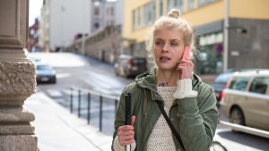Donna (Alina Tomnikov) kuuntelee kadulla puhelintaan toisessa kädessä hänellä on valkoinen keppi.