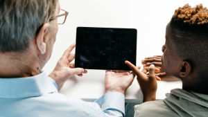 Lapsenlapsi osaa usein auttaa laitteiden käytössä. Lapsenlapsi neuvoo isoisää tabletin käytössä.